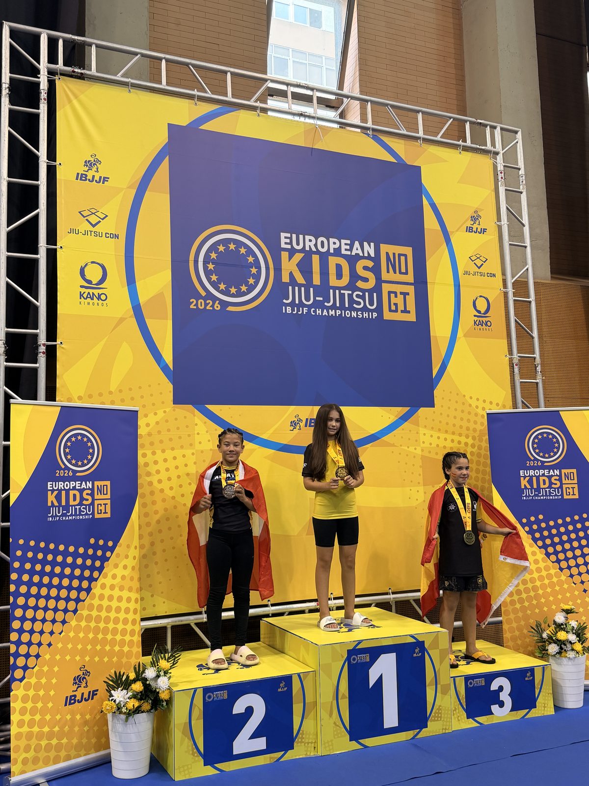Aylin with the silver medal and the Swiss flag on the podium of the IBJJF European Kids No-Gi Championship, Lisbon, October 2026.